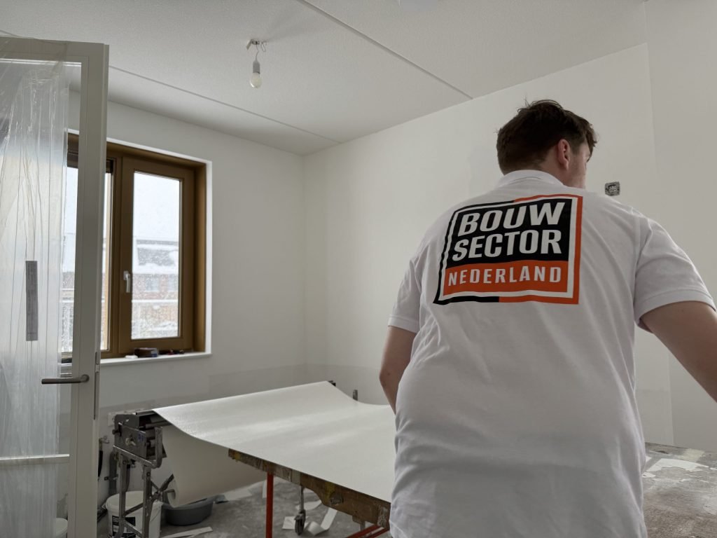 Behanger van Bouwsector Nederland bij de plaktafel met een baan vlies in een nieuwbouwkamer
