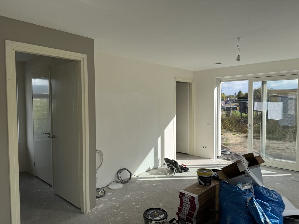 Woonkamer van een net opgeleverd nieuwbouwhuis met kale wanden en materiaal op de vloer