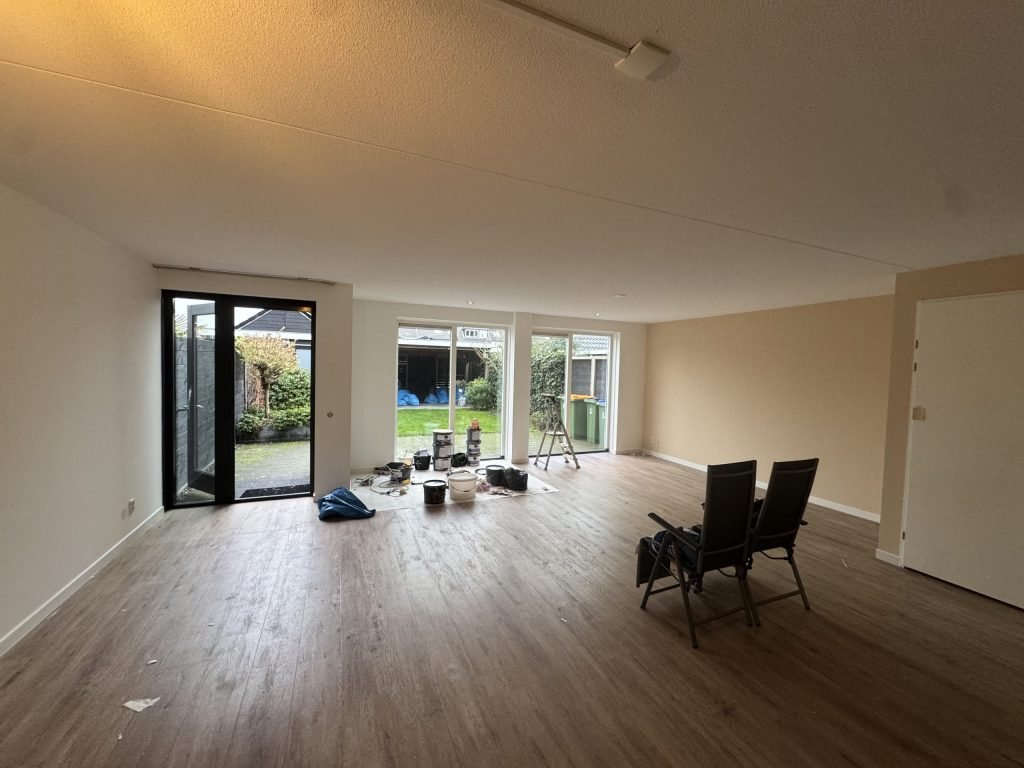 Woonkamer van een eengezinswoning met houten vloer en tuindeuren, klaar om te laten behangen