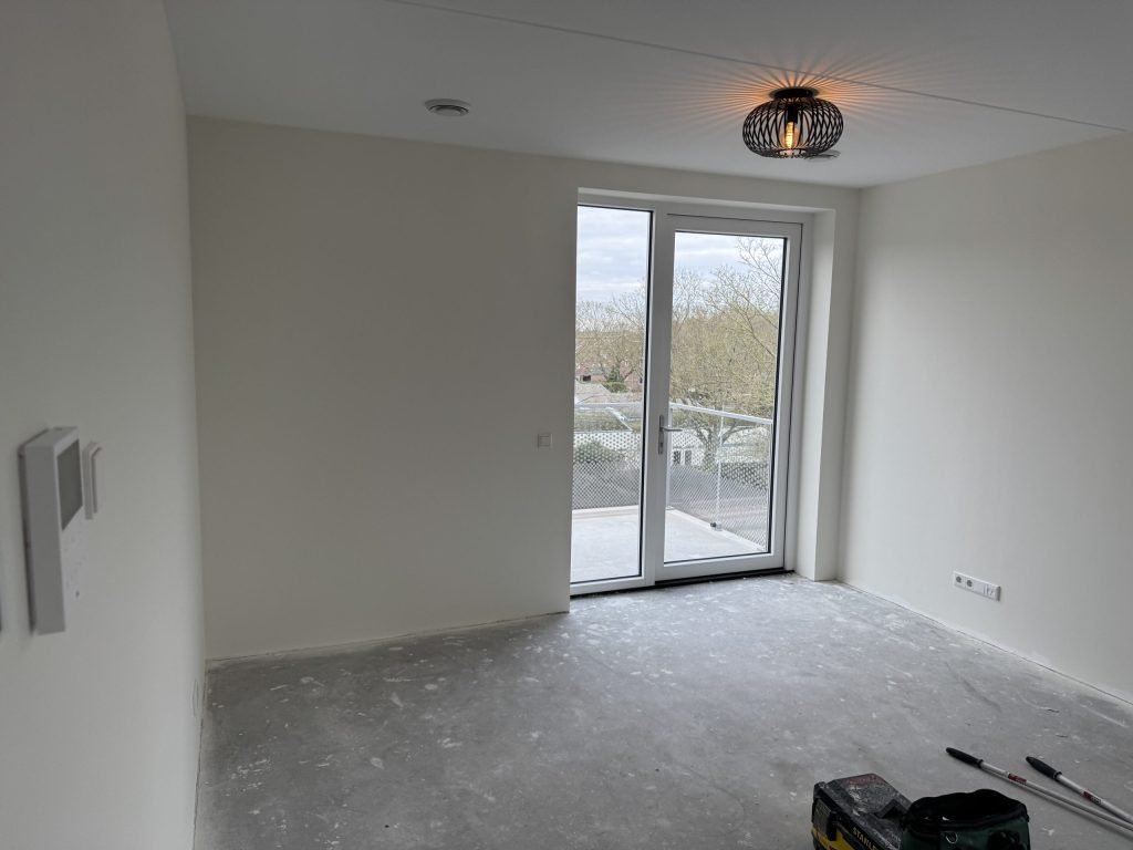 Lege kamer met strak afgewerkte witte wanden en een openslaande deur naar het balkon