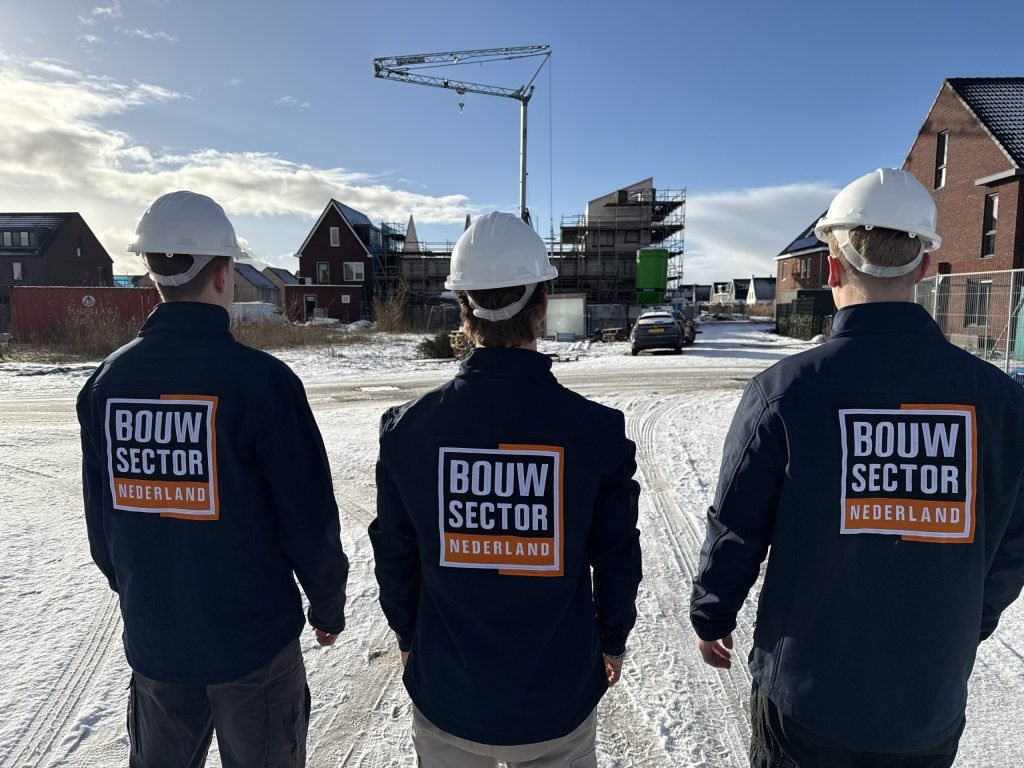 Drie medewerkers van Bouwsector Nederland met witte helm kijken naar een nieuwbouwwijk in aanbouw